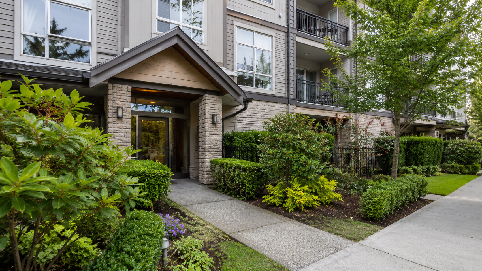 Modern apartment building entrance with landscaped walkway featuring native plants and shrubs, representing professional strata property management services for self-managed strata corporations in Surrey BC