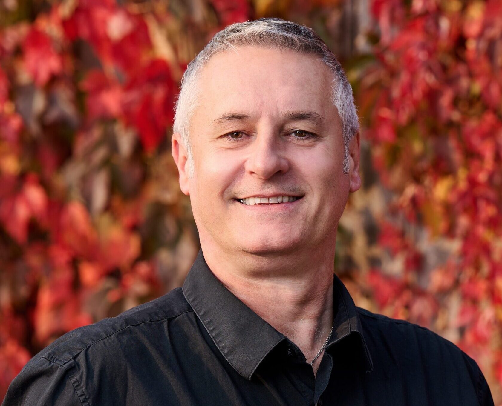 Phil Dougan, strata property management consultant in Surrey BC, smiling in front of autumn foliage